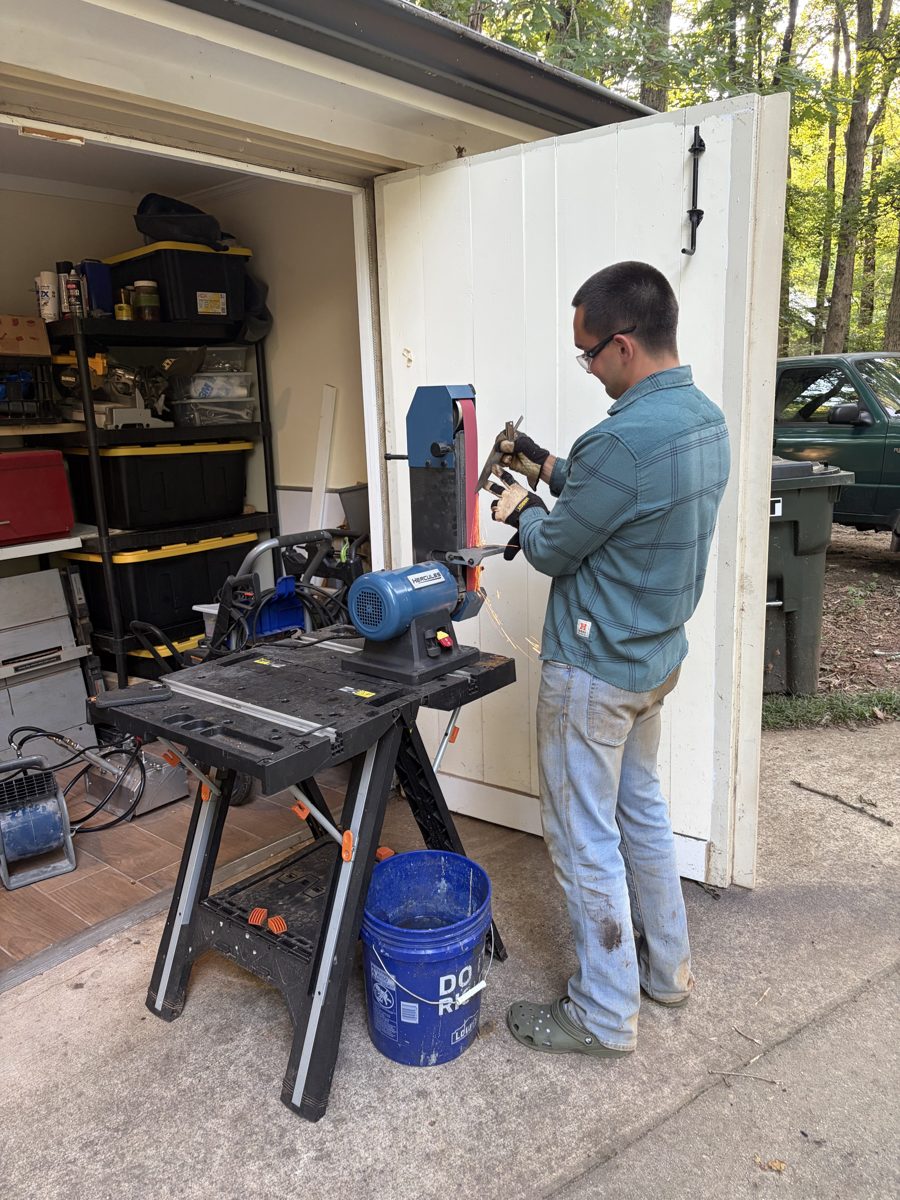 John Newland grinding a blade on a belt grinder outside the shop
