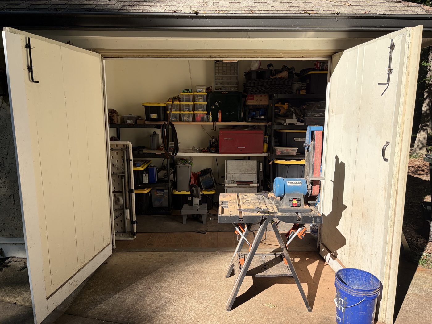 The shed where John is learning the craft, with shelves of tools, a belt grinder and a workbench